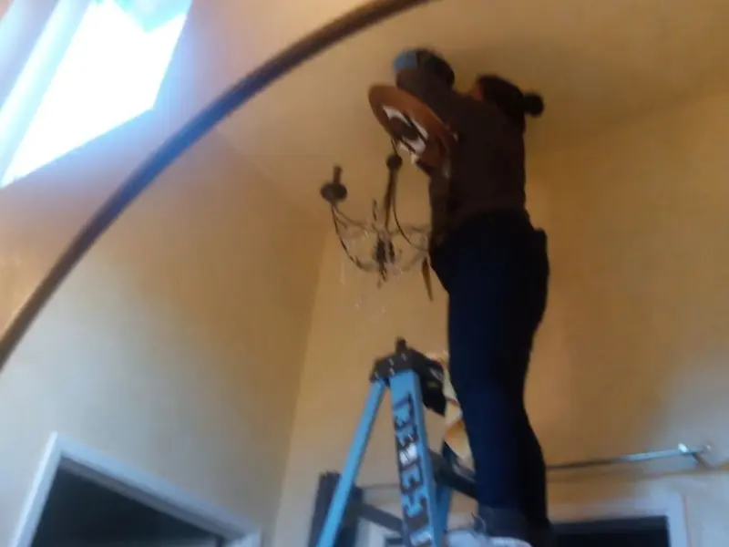 Electrician installing a chandelier in a Troy residence
